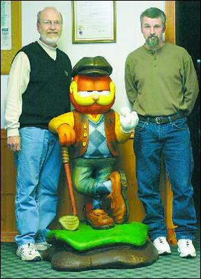 TEE TIME FOR GARFIELD- Arbor Trace Golf Course owner Jack Hart, left, and artist Scott Brown with the wood-carved Garfield created by Brown and designed by Garfield cartoonise and county resident Eric Reaves.